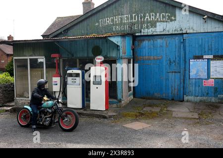 Motorradfahrer auf einem maßgeschneiderten Motorrad in einer alten, stillgelegten Garage in Lost Wenlock, Shropshire Stockfoto