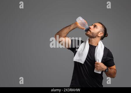 Ein Mann trinkt Wasser aus einer Flasche auf grauem Hintergrund Stockfoto