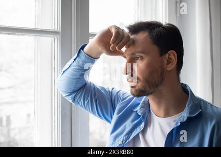 Mann, der aus dem Fenster blickt, mit der Hand auf dem Kopf Stockfoto