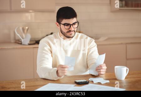 Mann, der am Tisch sitzt und Papier hält, mit Rechner Stockfoto