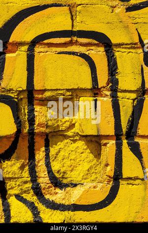 Gelbe Sprühfarbe, mit schwarzem Ornament, Kunst auf Ziegelwand. Vertikale Textur. Stockfoto