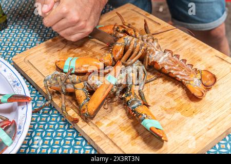 Die Hand des Mannes schneidet Hummerschwänze mit einem Messer auf einem Holzbrett Stockfoto