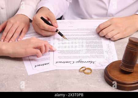 Mann und Frau unterzeichnen einen Heiratsvertrag am hellgrauen Tisch, Nahaufnahme Stockfoto