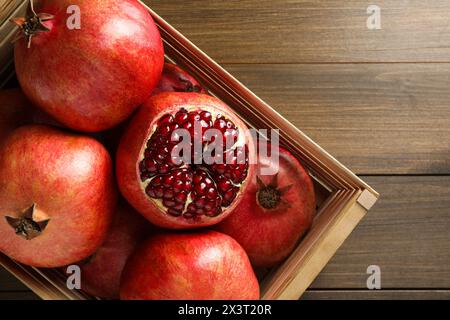 Reife Granatäpfel in Kiste auf Holztisch, Blick von oben Stockfoto