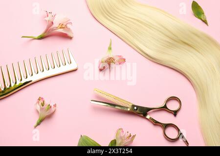 Friseurwerkzeuge. Blondes Haarschloss, Kamm, Schere und Blumen auf rosa Hintergrund, flach Stockfoto