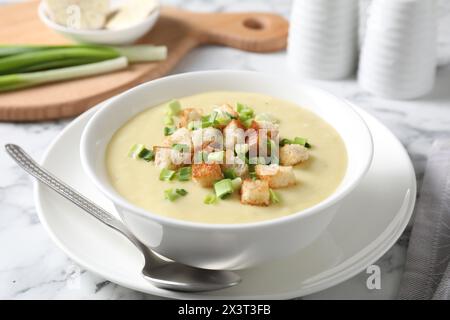 Leckere Kartoffelsuppe mit Croutons in Schüssel und Löffel auf weißem Marmortisch Stockfoto