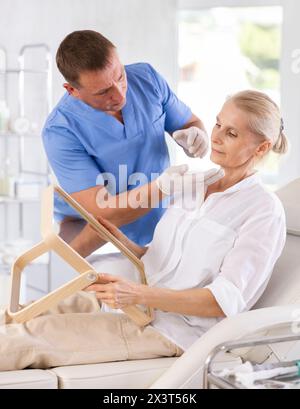 Männlicher Kosmetologe zeigt Ergebnisse der Gesichtsbehandlung bei älterer Frau Stockfoto