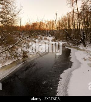 Eisbedecktes Wasser in einem Fluss im Winter, Sonnenuntergang auf einem Fluss, dessen Ufer mit Eis bedeckt sind Stockfoto