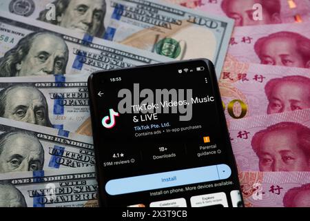 TikTok App auf dem Bildschirm des Smartphones, die auf US-Dollar und chinesische Yuan-Banknoten platziert ist. Stafford, Vereinigtes Königreich, 28. April 2024 Stockfoto