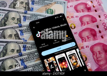 TikTok App auf dem Bildschirm des Smartphones, die auf US-Dollar und chinesische Yuan-Banknoten platziert ist. Stafford, Vereinigtes Königreich, 28. April 2024 Stockfoto