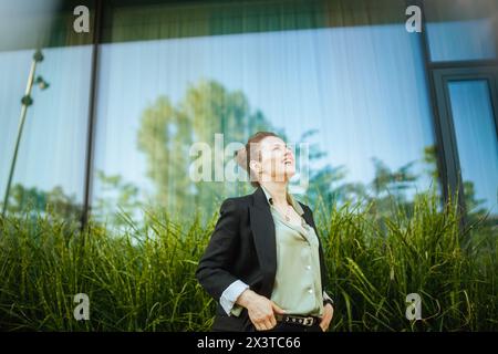 Glückliche moderne Arbeiterin der Nähe des Bürogebäudes in schwarzer Jacke. Stockfoto