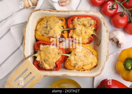 Köstliche gefüllte Paprika in Backform, Spachtel und Zutaten auf weißem, strukturiertem Tisch, flach gelegt Stockfoto