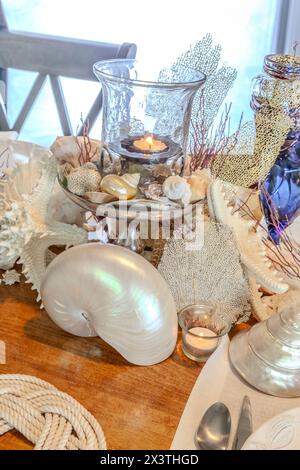 Muscheln- und Kerzendekoration auf einem nautischen Tisch mit natürlichen Farben und tiefem Blau. Stockfoto