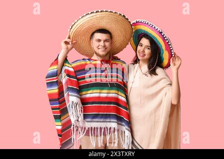 Schönes junges glückliches Paar in Sombrero-Hüten und Poncho auf rosa Hintergrund. Cinco de Mayo-Feier Stockfoto