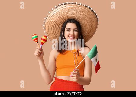 Schöne junge glückliche Frau im Sombrero mit mexikanischer Flagge und Maracas auf beigefarbenem Hintergrund. Cinco de Mayo-Feier Stockfoto