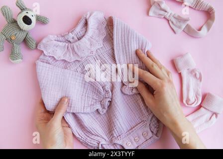 Rosafarbener Body mit Spielzeug gestricktem Hund, Socken und Stirnband. Set Babykleidung und Accessoires Sommer auf rosa Hintergrund. Fashion Neugeborene. Flach, oben Stockfoto