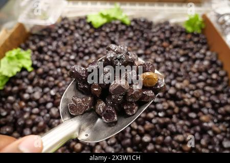 Schneidet schwarze Oliven mit einem Löffel in einer Schüssel, Stockfoto