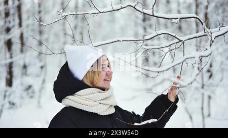 Ein Mädchen berührt sanft verschneite Äste im Wald. Stockfoto