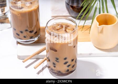 Iced Tapica Coffee Latte oder boba Pearl Bubbles Milchtee, asiatisches trendiges kaltes Kaffeegetränk mit Tapiokasseln und zerstoßenem Eis, auf weißem Marmorhintergrund Stockfoto