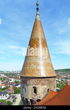 Oberer Teil des Buzdugan-Turms bei Corvin Castle: Gekacheltes Dach mit einer Statue eines Ritters auf der Spitze und die rumänische Stadt Hunedoara im Hintergrund. Stockfoto