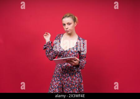 Eine Frau in einem lila Blumenkleid hält einen Tablet-Computer in der Hand Stockfoto