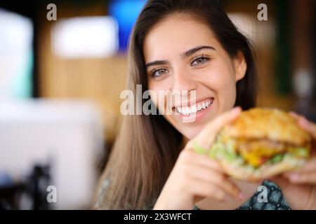 Porträt einer glücklichen Frau, die einen Burger in einem Restaurant hält und in die Kamera schaut Stockfoto