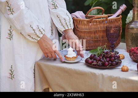 Frauenhände bereiten im Garten ein Sommerpicknick mit roten Äpfeln, frischen Beeren und Vintage-Gläsern vor. Biologisches Leben, natürliche Lebensmittel, Schönheit von allem Stockfoto