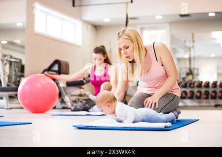 Bewegungsklasse für Babys. Eltern helfen Babys, die motorischen Fähigkeiten zu verbessern, die richtige Bewegung auf dem Fitball. Pädiatrie Physiotherapeut in der Spitzenklasse. Mütter Stockfoto