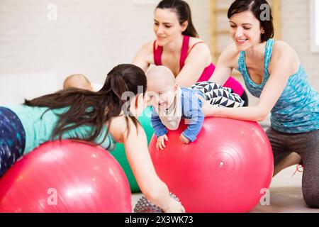 Bewegungsklasse für Babys. Eltern helfen Babys, die motorischen Fähigkeiten zu verbessern, die richtige Bewegung auf dem Fitball. Pädiatrie Physiotherapeut in der Spitzenklasse. Mütter Stockfoto