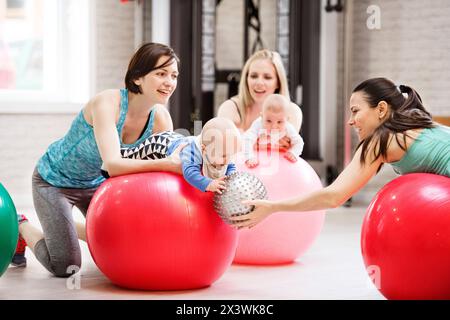 Bewegungsklasse für Babys. Eltern helfen Babys, die motorischen Fähigkeiten zu verbessern, die richtige Bewegung auf dem Fitball. Pädiatrie Physiotherapeut in der Spitzenklasse. Mütter Stockfoto