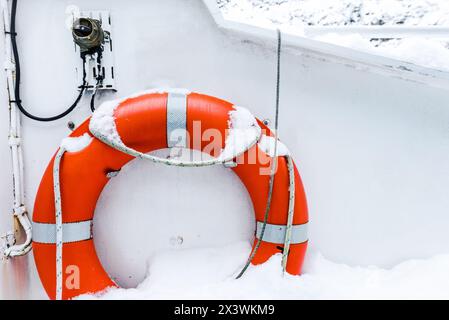 Rettungsring auf weißem Boot im Winter mit Schnee bedeckt. Sicherheitsausrüstung auf dem Boot. Orange Rettungsboje auf einem Segelboot Stockfoto