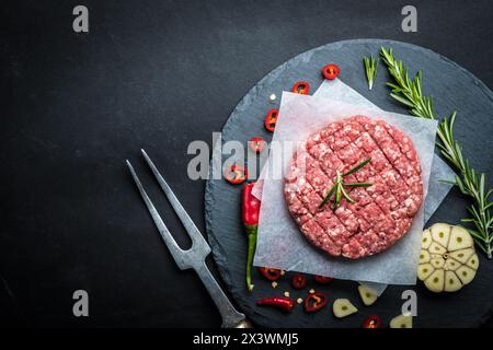 Bio-rohes Hackfleisch für die Herstellung von hausgemachten Burgern mit Rosmarin, Arten und Schnitzgabel auf Steinkochhintergrund, Draufsicht, Platz für Text Stockfoto