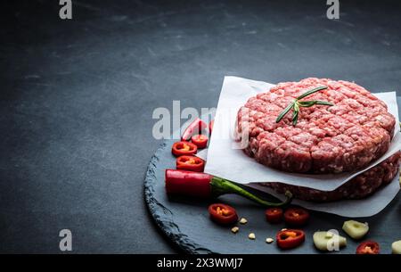 Rohes Burger-Cutlet aus Rinderfleisch mit Knoblauch und Rosmarin auf schwarzem Hintergrund mit Kopierfläche Stockfoto