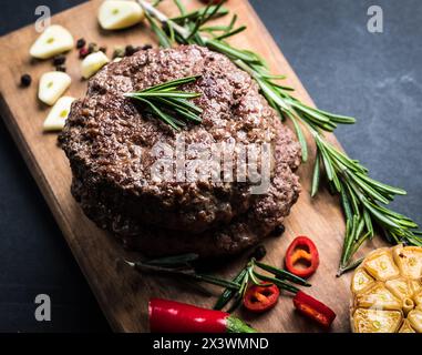 Köstliches Beef Burger Steak mit Gewürzen und Kräutern auf Schneidebrett und Schieferhintergrund Stockfoto