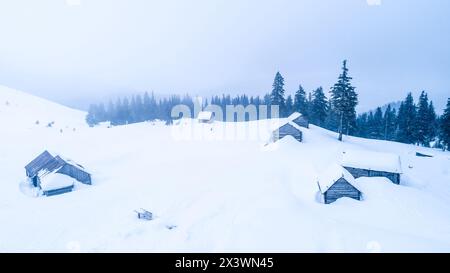 Holzhütten im tiefen Schnee auf dem Bergtal im Winter, Blick von oben. Schneebedeckte Chalets für Touristen in den Winterbergen der ukrainischen Karpaten Stockfoto
