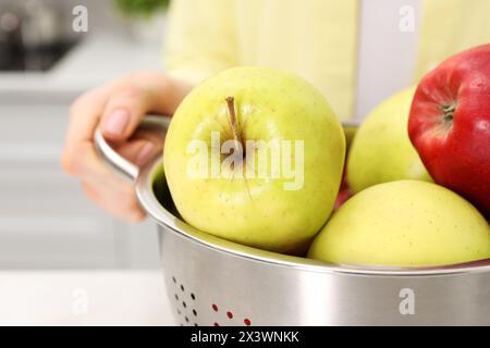 Frau, die Sieb mit frischen Äpfeln am Tisch drinnen hält, Nahaufnahme Stockfoto