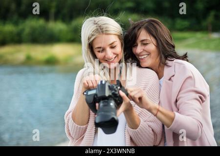 Erwachsene Tochter, die Mutter beibringt, wie man Fotos mit professioneller Kamera macht, erklärt Technik, lacht. Muttertagskonzept. Stockfoto