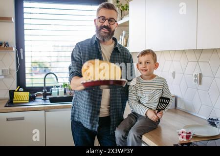 Junge, der Vater hilft, Pfannkuchen zu machen. Sohn, der sieht, wie Vater Pfannkuchen umwirft. Vatertagskonzept. Stockfoto