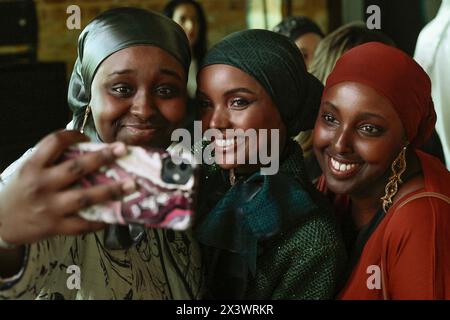 Istanbul, Türkei. April 2024. Zwei Mädchen afrikanischer Herkunft beim Selfie mit Halima Aden (C) gesehen. Das somalisch-amerikanische Model Halima Aden trifft die Öffentlichkeit und Influencer während des Vortrags „eine inspirierende Geschichte: Halima Aden“ am dritten Tag der Modest Fashion Week in der Fisekhane Gallery, Istanbul. Quelle: SOPA Images Limited/Alamy Live News Stockfoto