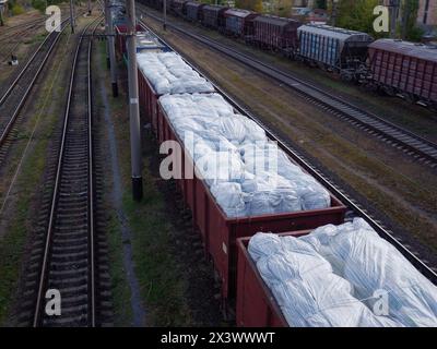 Ein Güterzug mit Güterwagen ohne Dächer, beladen mit riesigen weißen Säcken und wartet am Bahnhof in Kiew-Stadt, Ukraine. Stockfoto