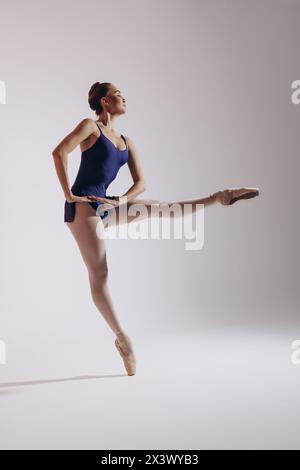 Junge Ballerina im Body und spitzenschuhen tanzen vor weißem Hintergrund. Anmutig schöne Ballerina. Ballettkunst, Anmut, Flexibilität, Bewegung. Stockfoto