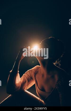 Porträt der jungen müden Ballerina, die nach der Probe sitzt und entspannt, vor dem Hintergrund des Rampenlichts. Anmutig schöne Ballerina. Ballettkunst, Stockfoto