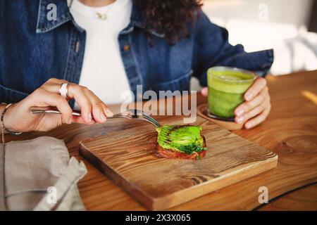 Feminine Hände halten Avocadotoast und grünen Smoothie in einem Restaurant und zeigen vegane gesunde Speisen. Stockfoto