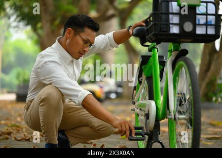 Attraktiver männlicher Büroangestellter, der sein Fahrrad im öffentlichen Park repariert Stockfoto