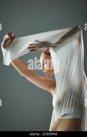 Eine junge Ballerina in einem weißen Kleid hält anmutig ihren Schleier über dem Kopf. Stockfoto