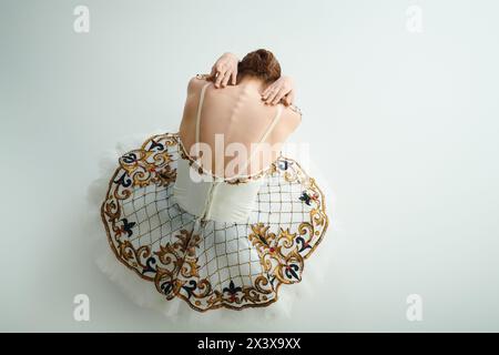 Eine anmutige Ballerina in einem weißen Kleid sitzt auf dem Boden und zeigt ihr Talent. Stockfoto