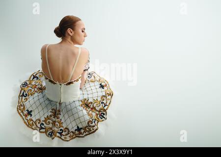 Eine junge, schöne Ballerina in einem fließenden weißen Kleid sitzt elegant. Stockfoto