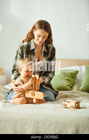 Eine junge Mutter spielt fröhlich mit ihrer Kleinkind-Tochter auf einem gemütlichen Bett und schafft zusammen herzzerreißende Erinnerungen. Stockfoto