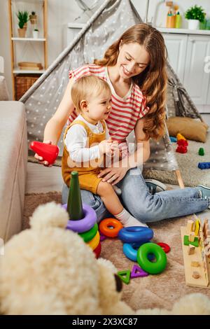 Eine junge Mutter spielt fröhlich mit ihrer Kleinkind-Tochter zu Hause auf dem Boden, verbindet und schafft zusammen glückliche Erinnerungen. Stockfoto