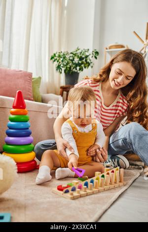 Eine junge Mutter spielt fröhlich mit ihrer Tochter auf dem Boden, verbindet sich und schafft zusammen bleibende Erinnerungen. Stockfoto